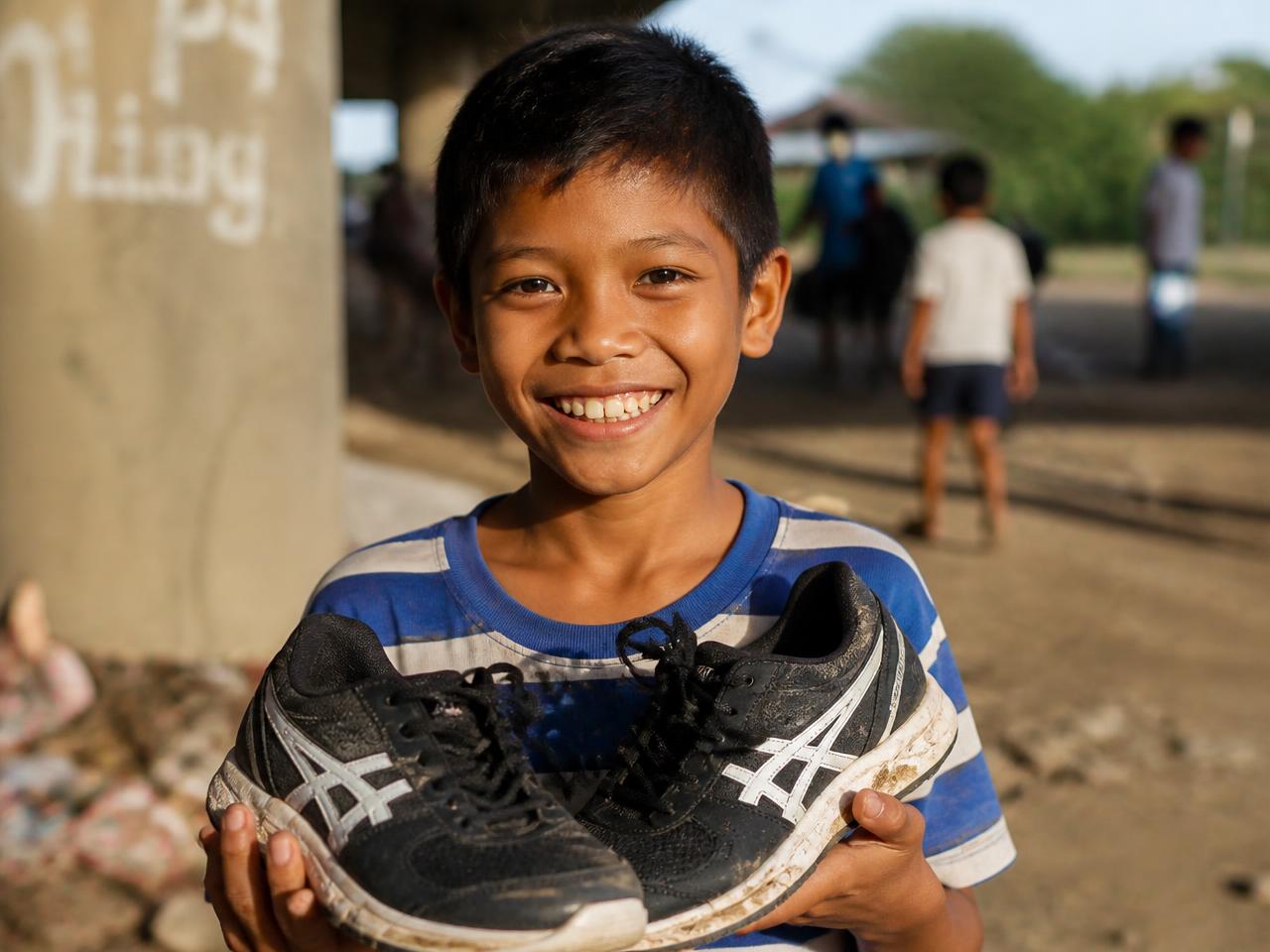 A boy holding a pair of donated sneakers