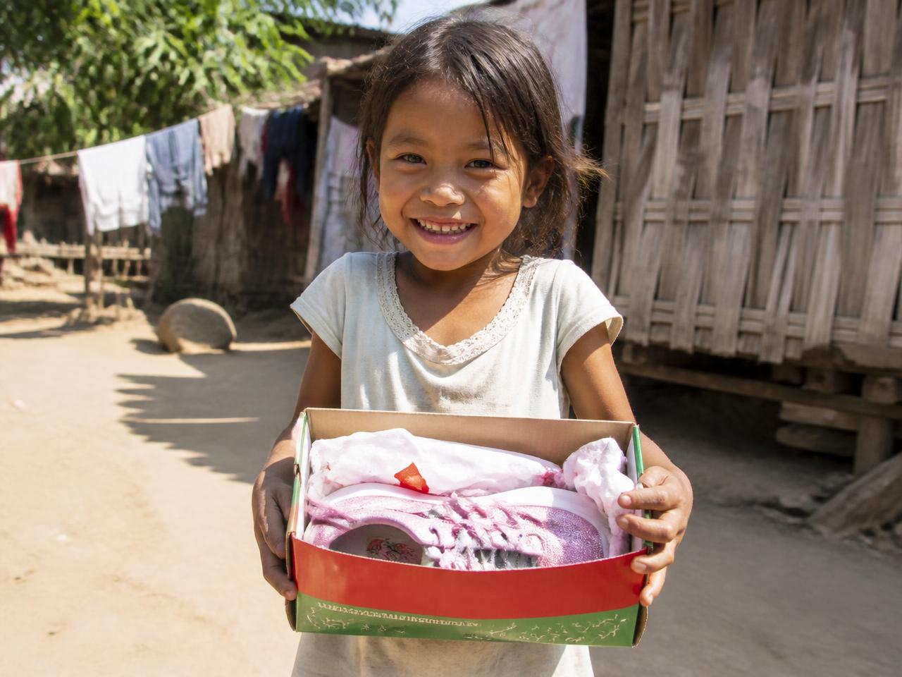 A smiling girl holding a new-to-her shoebox at a donation event